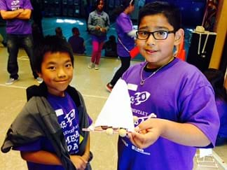 A photograph shows two young boys in a school, smiling and holding a sail car.