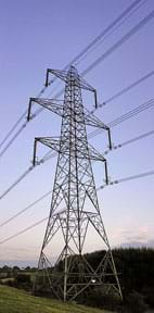 A photograph shows a very tall tower made from metal trusses, supporting more than six sets of wires travelling to/from other towers across the landscape near Aust, England, UK.