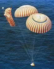 A photograph shows the Apollo 14 capsule descending into the ocean for splashdown with two of its three red and white stripped parachutes fully inflated.