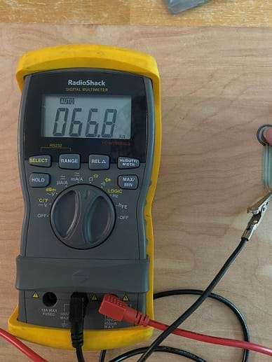 An index finger is pressing on a round force-sensitive resistor that is attached with alligator clips to a yellow multimeter. The multimeter is set to AUTO ranging resistance and reads 0.518 k on the display.