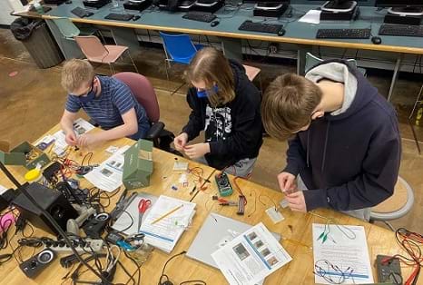 Three learners are testing the resistance of force-sensitive resistors using breadboards and multimeters.