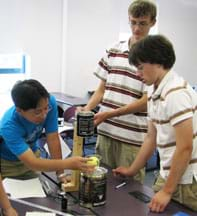 Photo shows three teenagers around a classroom table working on a device.