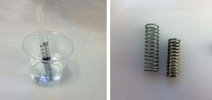Two photos: (left) A spring placed inside a clear, plastic 20 ml syringe is filled partway with water and rests inside a clear plastic cup filled halfway with water so the bottom portion of the syringe is submerged. (right) Two metal springs, one 3 cm in length, the other 3.5 cm in length, with different diameters and thicknesses.