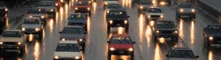 Photo shows six lanes of cars on a highway in the rain.