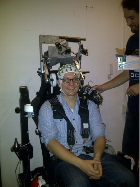 A man sitting down and having an electroencephalogram (EEG) measured—he is wearing a white cap with several electrodes.