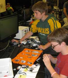 A photograph shows two boys working with LEGO NXT parts and pieces at a lab bench.