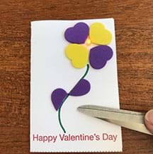 Photograph of closed Valentine’s card with a pair of scissors pushing down on the card to light it up.
