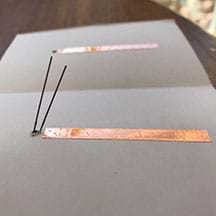 Photograph of the inside of the cardstock element.  The LED has been pushed through the hole from the OUTSIDE cover. The LONG lead of the LED is towards the top of the card and the shorter wire is closer to the copper tape.
