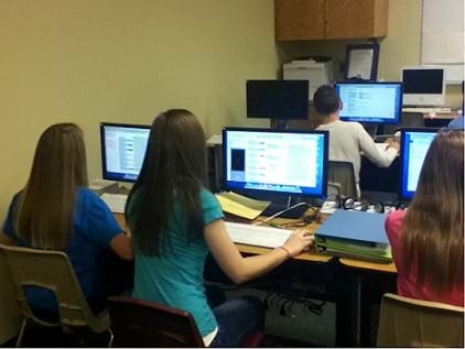 A photograph shows four students working at computers.