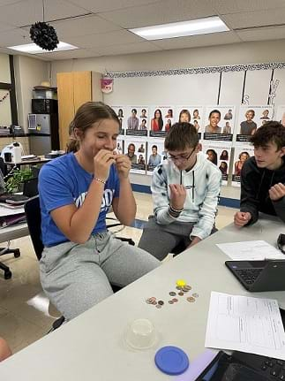 A student with their eyes closed is using the sense of smell to figure out the value of the coin.