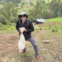 A photo of one of the curriculum authors (Doug) atop the hill, holding a bag of the material that was moved on the hill. At the bottom of the hill is the reservoir being used to collect water for irrigation.