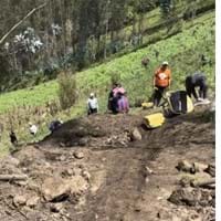 Photo of the minga from Yambiro working on a community project. They are moving bags of materials on the hill. The image shows the incline of the hill.
