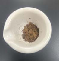 A photo of a mortar with a crushed-up, brown, dried leaf-like substance in it.