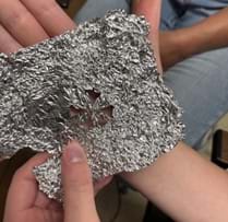 A photo showing a student holding aluminum foil with a pattern cut into it.