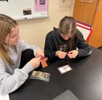 A photo showing two high school students using notecards and copper tape to build a logic gate.