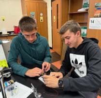 A photo showing two high school students using a breadboard, wires, and other electrical components to build an integrated logic circuit.