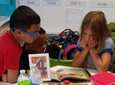 A photograph of three students, a girl and two boys, looking at a book about insects.