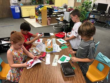 Four children sit around a table using craft materials to create what they think germs would look like under a microscope.