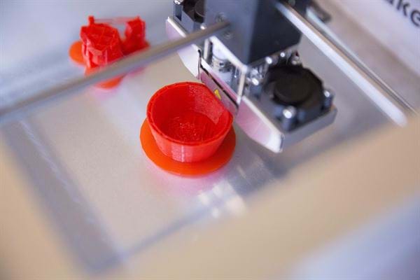 A 3D printer is printing a plastic part out of red filament.
