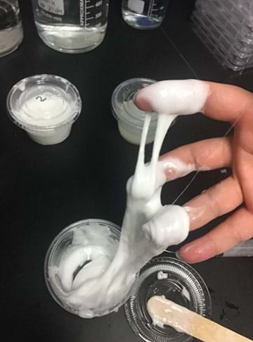 An image of a person’s fingers covered in slime against a black background.
