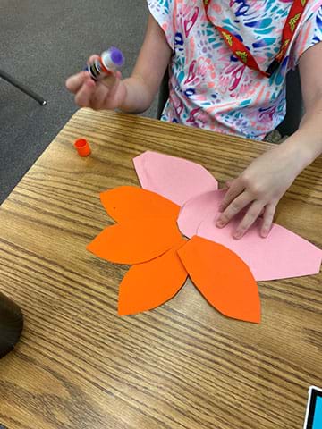 A student creating models of flowers out of construction paper using a glue stick. 