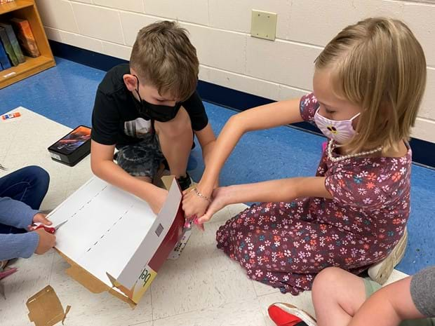 Two students cut cardboard materials.