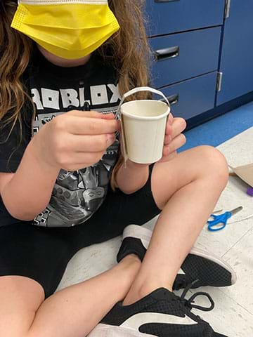 A student uses an old water cup and a small strip from a tissue box to make a snack holder.