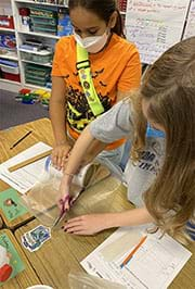 Students are working together to measure and cut wax paper to line their water bottle holder within order to make it water resistant.