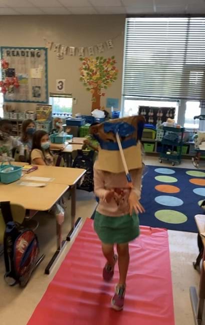 A child dressed like animal walking down the catwalk. The child is wearing a mask made of cardboard with a long tube taped to the front to create a trunk. 