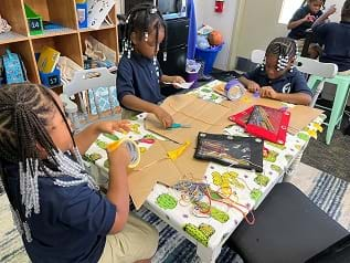 Elementary students work on their designs at a group table.