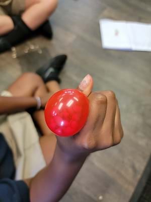 Photo of a completed fidget tool prototype. A student holds a red balloon slightly inflated and filled with beads. 