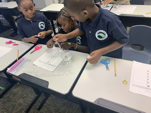 Three students work as a team to test their designs and record their results at a classroom desk. 