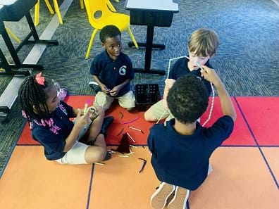 Four students are being observed manipulating straws and chenille sticks/pipe cleaners to create their design.