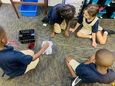 Four students are being observed manipulating the spiderweb, straws and chenille sticks/pipe cleaners to create their design.