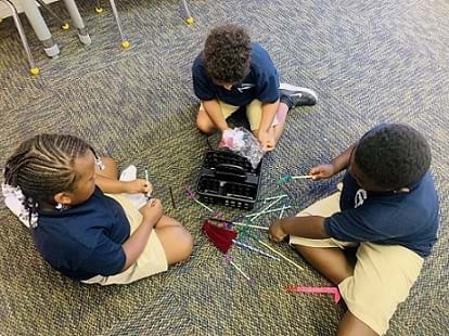 Three students are being observed manipulating their spiderweb, straws and chenille stick/pipe cleaners to create their design.