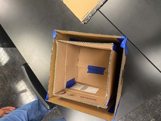 An overhead view of a small cardboard box inside a larger cardboard box. The effect is a box with interior and exterior walls.