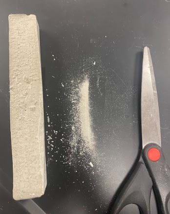 The image shows the solubility station. Scissors can be used to shave a small amount of the concrete sample into powder. This concrete powder can then be used to test if the concrete sample is soluble in water. 