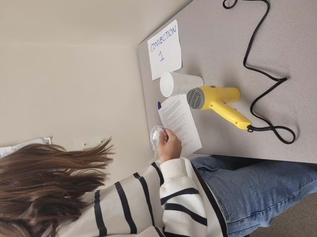 A student uses a hair dryer to demonstrate convection.