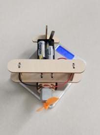 A wooden model airplane with batteries sits on a small digital scale.