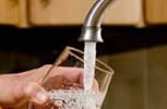 A photograph shows an adult hand holding a glass under a silver metal kitchen tap as it fills with clear water.