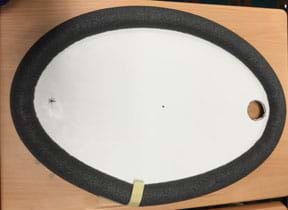 A photograph looks down on an elliptical pool table made of a white surface with a hole at one end a star at the other, and edges made of a black rounded foam tube material.