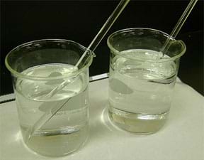 Photo shows two beakers each filled with clear liquids and a stirring rod in each. In one beaker you can see the entire stirring rod; in the other beaker, the part of the stirring rod in the liquid is not visible.