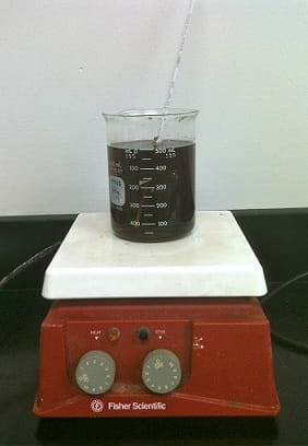 A photo show a beaker of dark brown liquid on hot plate with the heating dial turned to level 3 of 10.
