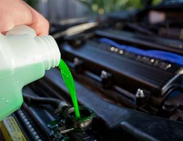 The image shows green-colored engine coolant being poured into a car's radiator.