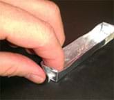 Photo shows a hand pinching flat the end of what looks like a long tray made of silvery foil.