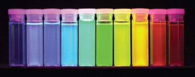 Photo shows a row of 10 stoppered square glass jars, each with glowing content in a different ROYGBIV (red to violet) rainbow spectrum of colors.
