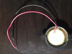 A photograph shows a white ceramic disc with larger gold metal disc underneath it. A red wire is soldered to the white part and a black wire to the gold part.