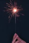 Photo shows a hand holding a burning sparkler.