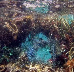 Debris of fishing nets, plastic and other colored trash surround a small opening underwater that a person could swim through. Found in the waters of the Northwestern Hawaiian Islands Marine National Monument.
