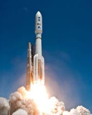 A photograph shows a tall white rocket pointed upwards into the blue sky, with flames and clouds of white exhaust. It's an Atlas V rocket with NASA's Juno spacecraft launching from Cape Canaveral Air Force Station in Florida. 